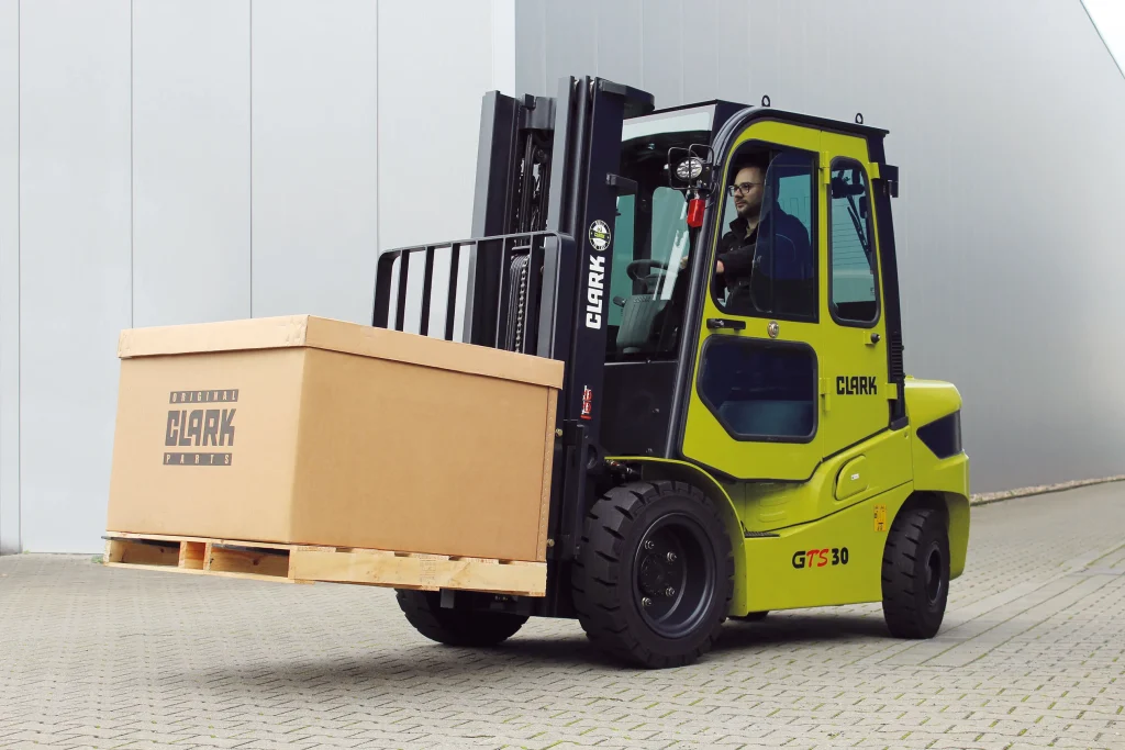 Carretilla elevadora Clark GTS 30 transportando una caja sobre un palet en un entorno industrial.