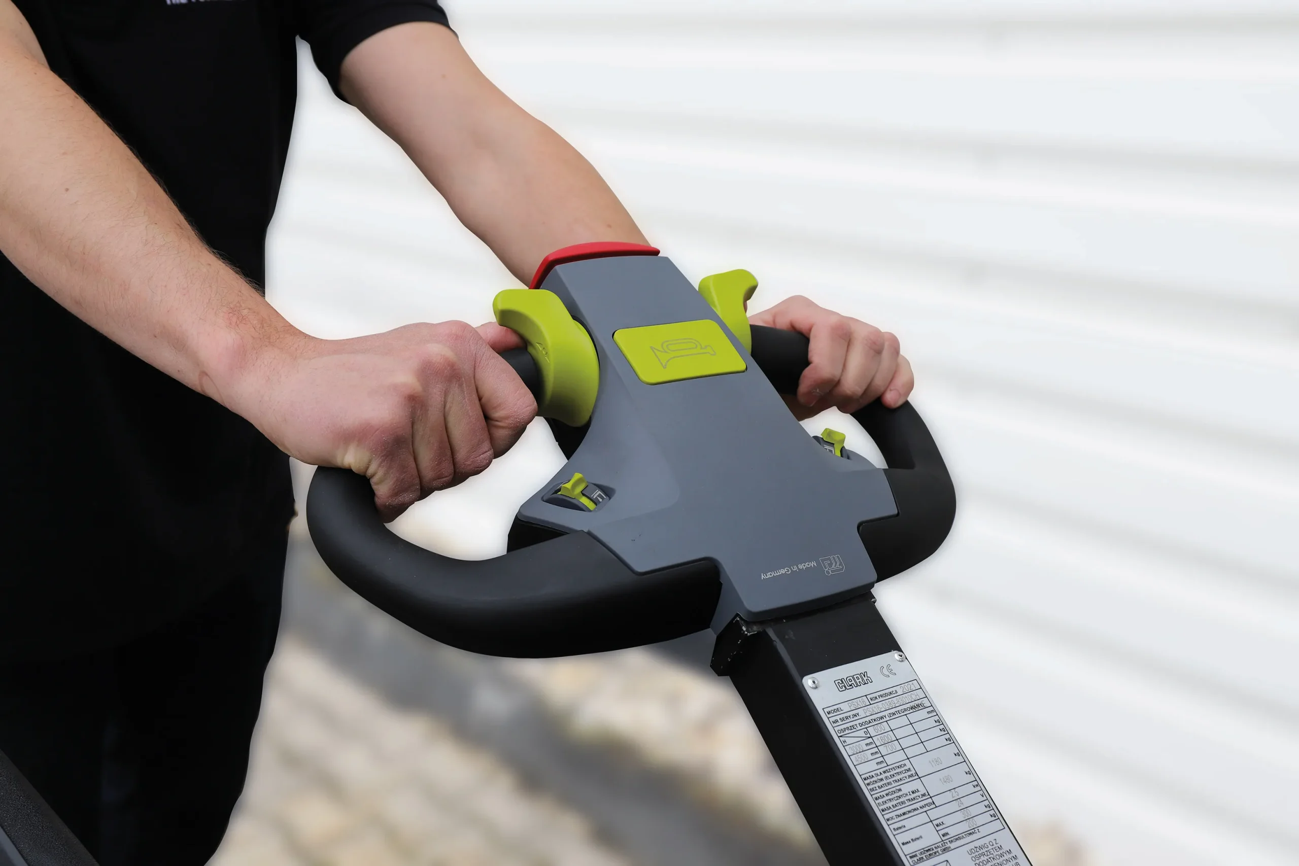 Primer plano de las manos de un operario sujetando un timón de control ergonómico de un apilador eléctrico, junto a un texto que detalla sus ventajas operativas.