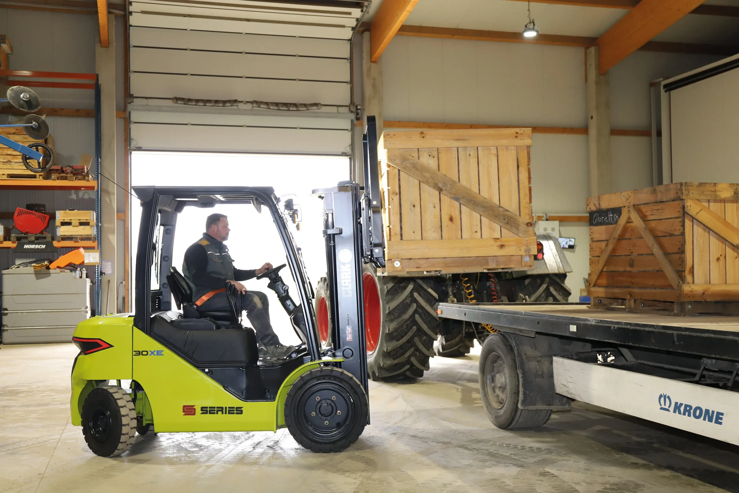 Carretilla elevadora Clark 30XE transportando una caja de madera en un almacén industrial hacia un remolque.