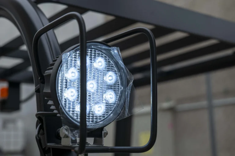 Foco LED en carretilla elevadora con rejilla de protección en un entorno industrial.
