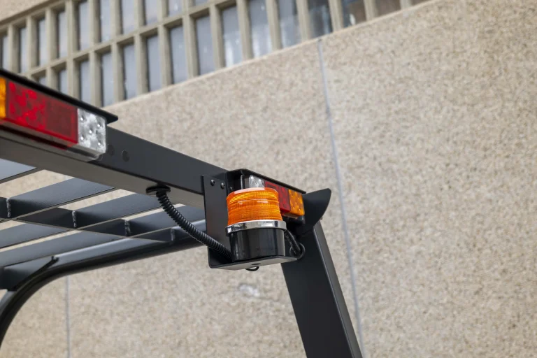 Luz de advertencia ámbar y luces traseras en la parte superior de una carretilla elevadora en un entorno industrial.
