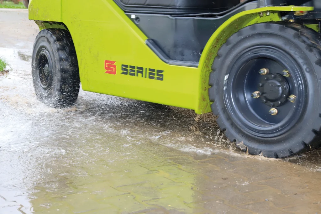 Primer plano de la rueda de la carretilla elevadora CLARK S Series atravesando un charco de agua, demostrando su resistencia en condiciones húmedas.