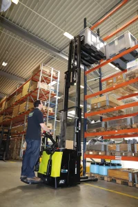 Apilador eléctrico elevando una carga a gran altura en un pasillo de almacén con estanterías industriales