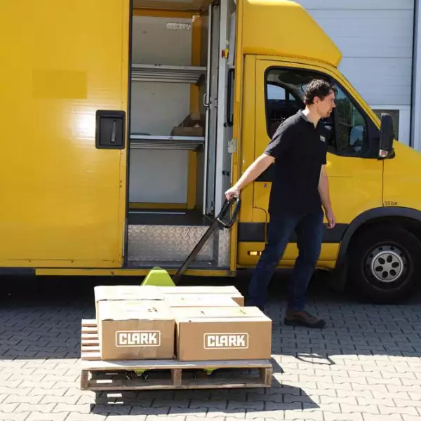 Trabajador usando transpaleta manual CLARK para descargar cajas de una furgoneta amarilla.