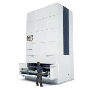 Imagen de un sistema de almacenamiento vertical automatizado llamado Modula Lift. Muestra una gran estructura blanca con puertas corredizas y un operario trabajando en la parte frontal.