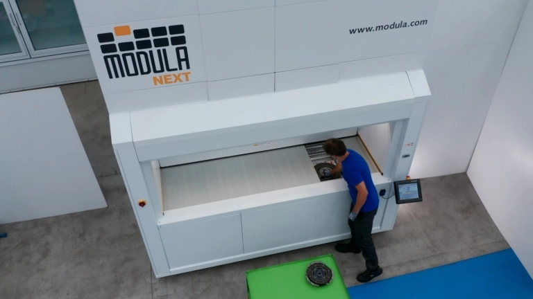Un operario interactúa con el sistema de almacenamiento vertical Modula NEXT en un entorno industrial.