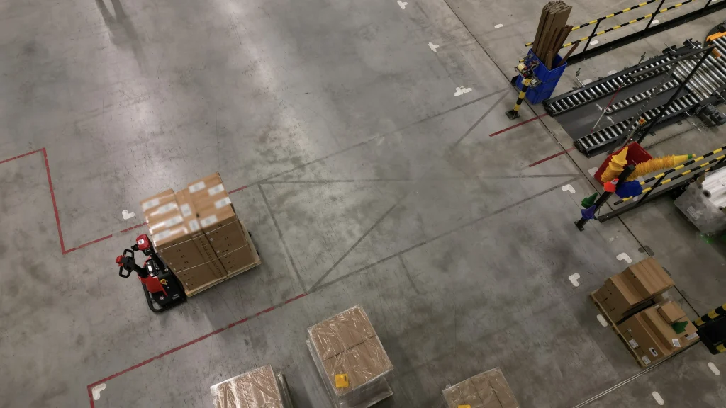 Vista aérea de una transpaleta eléctrica XP15 transportando una tarima de cajas en un almacén industrial.