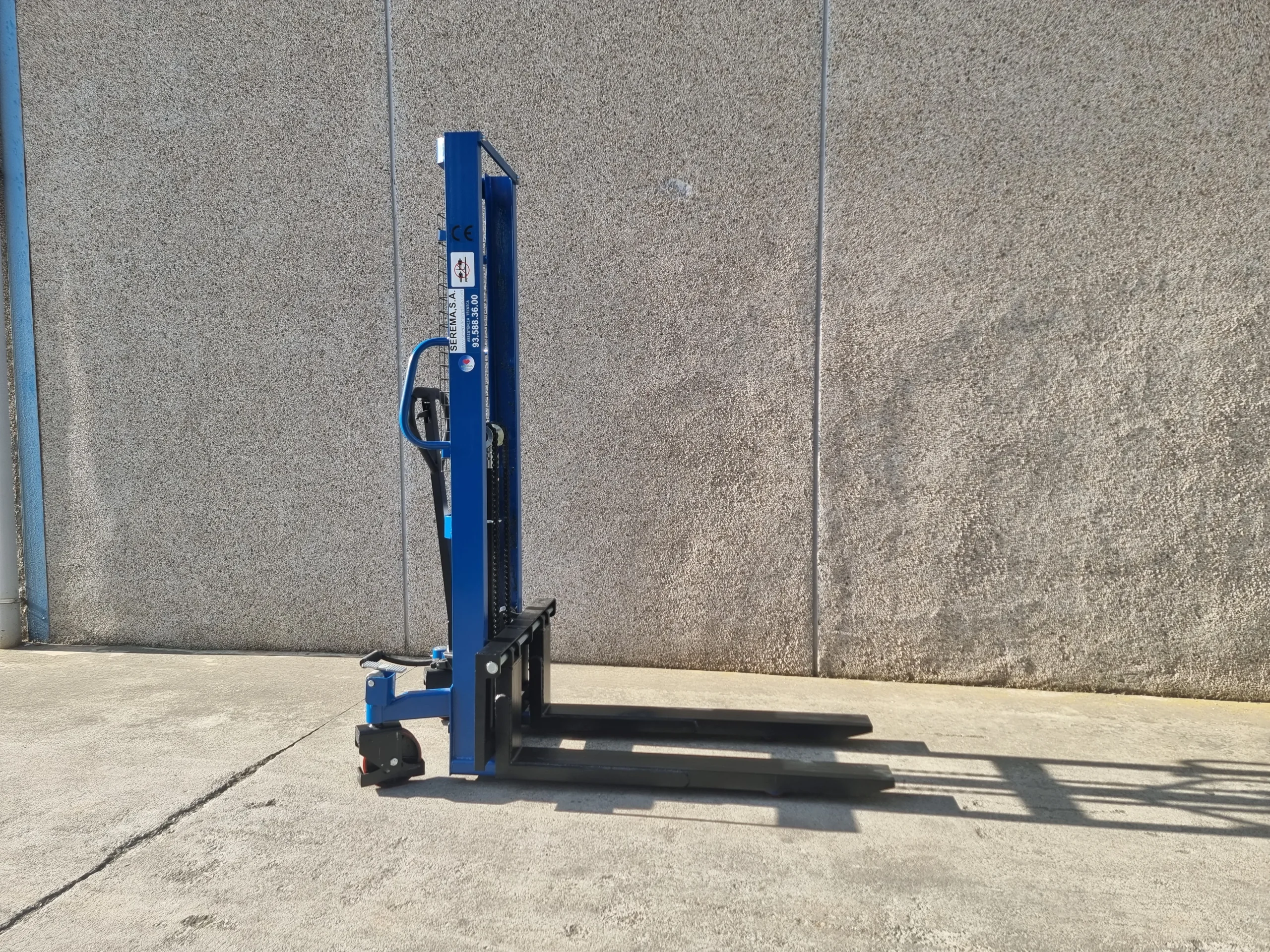Apilador manual azul estacionado sin carga en un entorno de almacén, listo para ser utilizado.