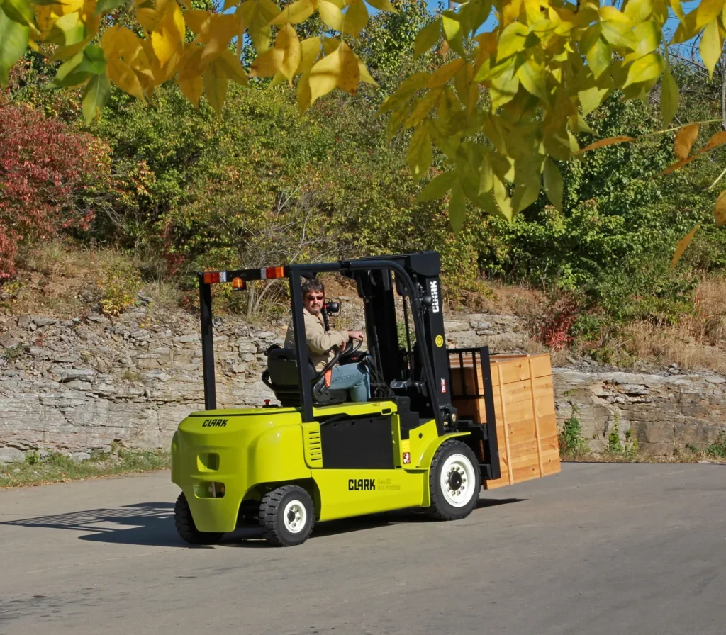 Carretilla elevadora CLARK GEX40 transportando una caja de madera en un entorno exterior rodeado de vegetación y árboles otoñales.