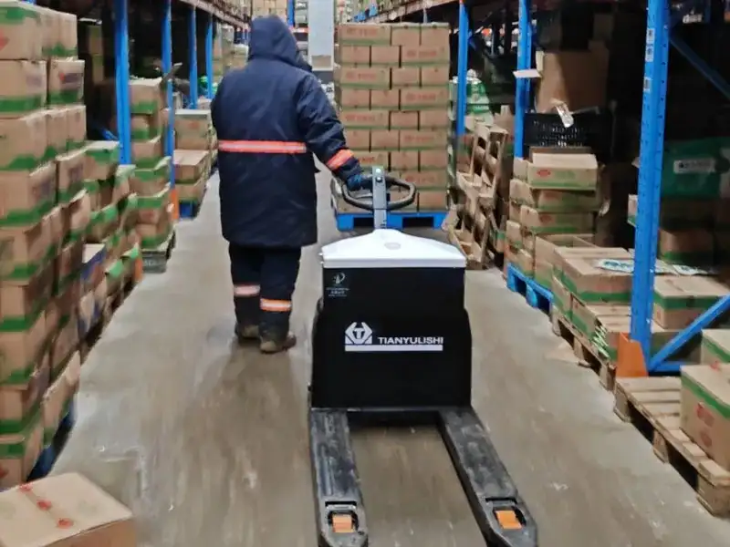 Operari amb roba de protecció tèrmica utilitzant la transpaleta elèctrica en un magatzem de congelació i producció alimentària.