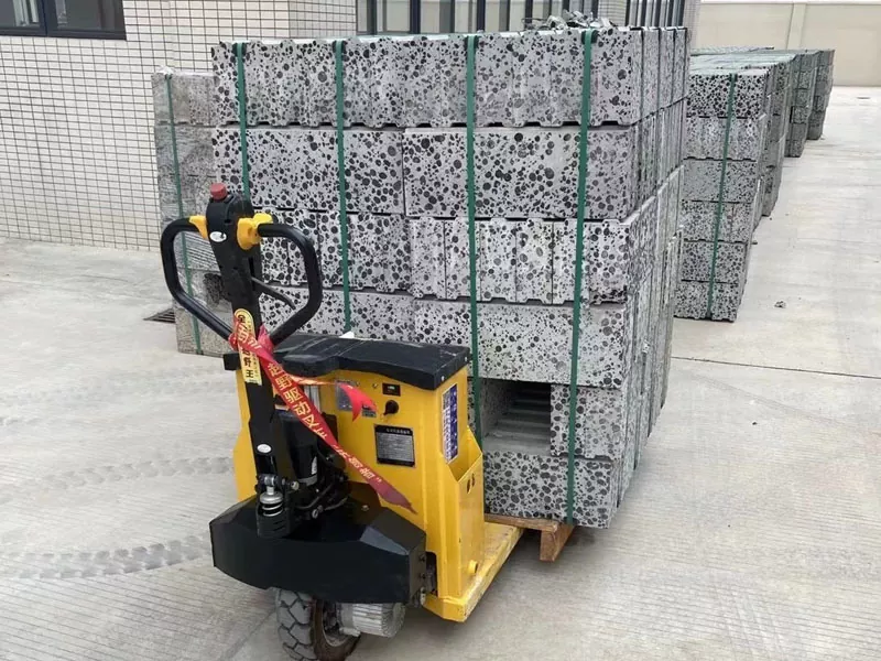 Transpaleta elèctrica groga TYA30 transportant un palet carregat amb blocs de pedra o edificació en un entorn industrial.